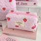 1PC Pink Strawberry Women Cosmetic Quilted Bag on a table with a pink book and other cosmetic items.