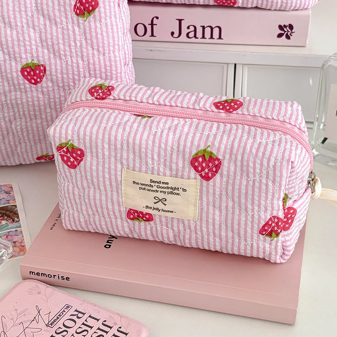 1PC Pink Strawberry Women Cosmetic Quilted Bag on a table with a pink book and other cosmetic items.